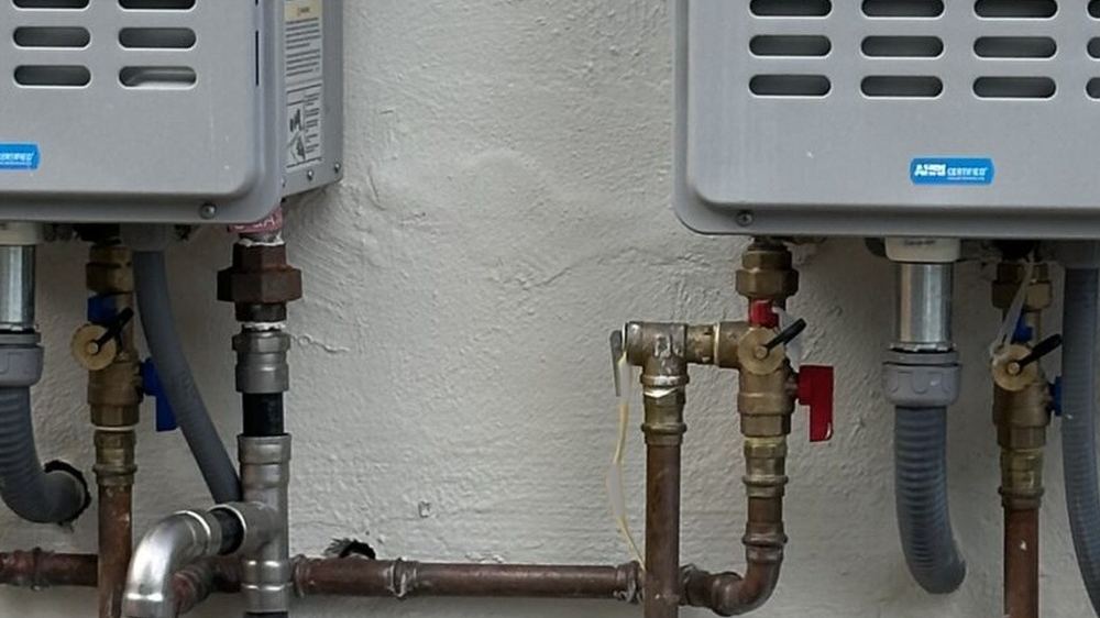 Two outdoor tankless water heaters with copper and gas piping on a stucco wall