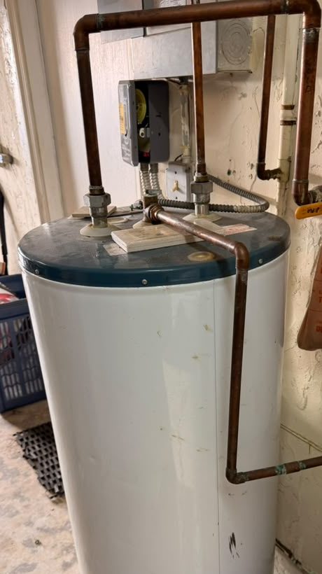 Before: an old white tank water heater with a teal top, connected with rigid copper pipe, in a Miami utility room
